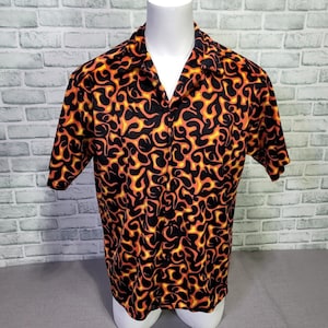 Puede incluir: Una camisa negra de manga corta con botones y un estampado de llamas naranja y amarillo.