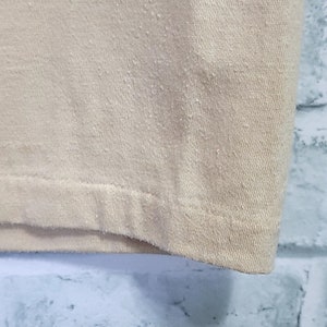 May include: Close-up of the bottom hem of a beige t-shirt. The fabric is a soft, knit material.