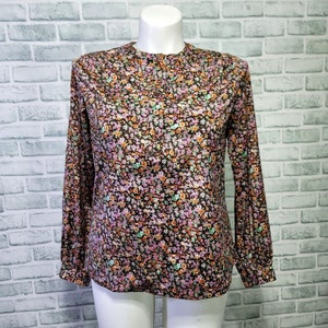 May include: A long-sleeved blouse with a black background and a small floral print in shades of pink, orange, green, and white.