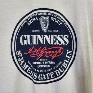 May include: A black and white circular logo for Guinness beer. The logo features the text "BREWED BY ARTHUR GUINNESS SON & CO. (DUBLIN) LTD." and "ST. JAMES'S GATE DUBLIN". The logo also features the text "GUINNESS" in a large white font and the signature "Arthur Guinness" in red.
