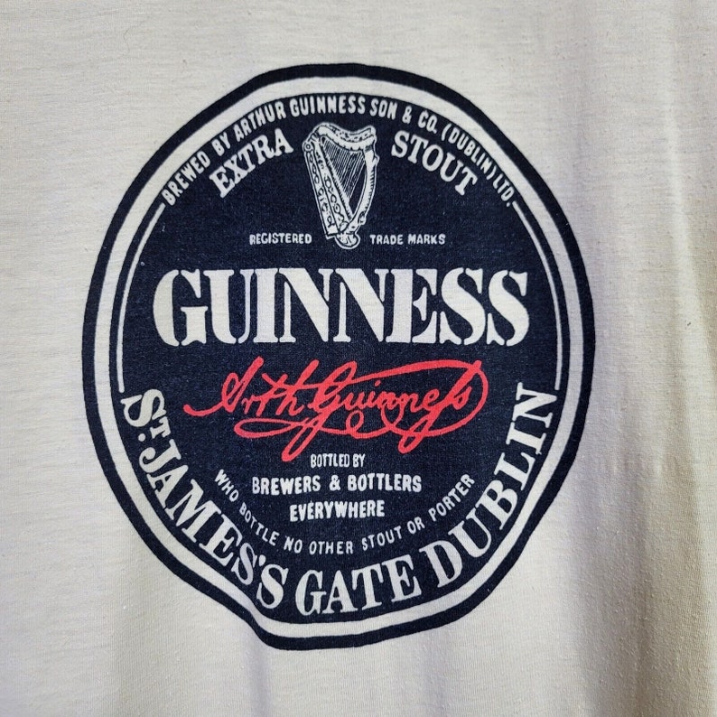 May include: A black and white circular logo for Guinness beer. The logo features the text "BREWED BY ARTHUR GUINNESS SON & CO. (DUBLIN) LTD." and "ST. JAMES'S GATE DUBLIN". The logo also features the text "GUINNESS" in a large white font and the signature "Arthur Guinness" in red.
