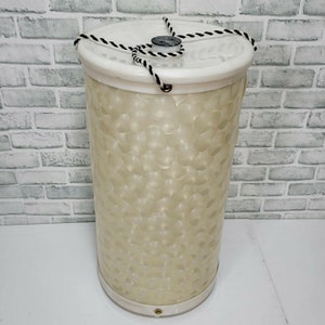 Könnte beinhalten: Ein weißer Kunststoff-Aufbewahrungsbehälter mit einem schwarz-weißen Seilgriff. Der Behälter hat eine strukturierte Oberfläche mit kleinen, erhabenen Kreisen.