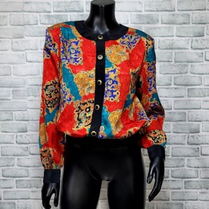 May include: A red, blue, and gold patterned blouse with a black button-up front. The blouse has long sleeves and a fitted silhouette.