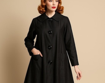 May include: A black coat featuring a wide collar, long sleeves, and a flared silhouette. The garment includes four large, round black buttons down the center front and two patch pockets on the front. The coat has a smooth texture and a structured fit.