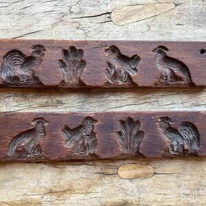 May include: Two wooden cookie cutters with carved designs. The top cutter has a rooster, two birds, and a leafy design. The bottom cutter has a rooster, two birds, and a leafy design.