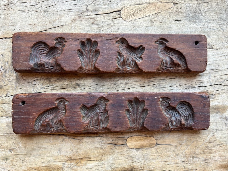 May include: Two wooden cookie cutters with carved designs. The top cutter has a rooster, two birds, and a leafy design. The bottom cutter has a rooster, two birds, and a leafy design.