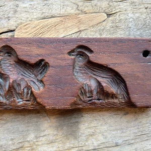 May include: Antique wooden cookie cutter with two bird designs. The cutter is brown and has a hole in the top.