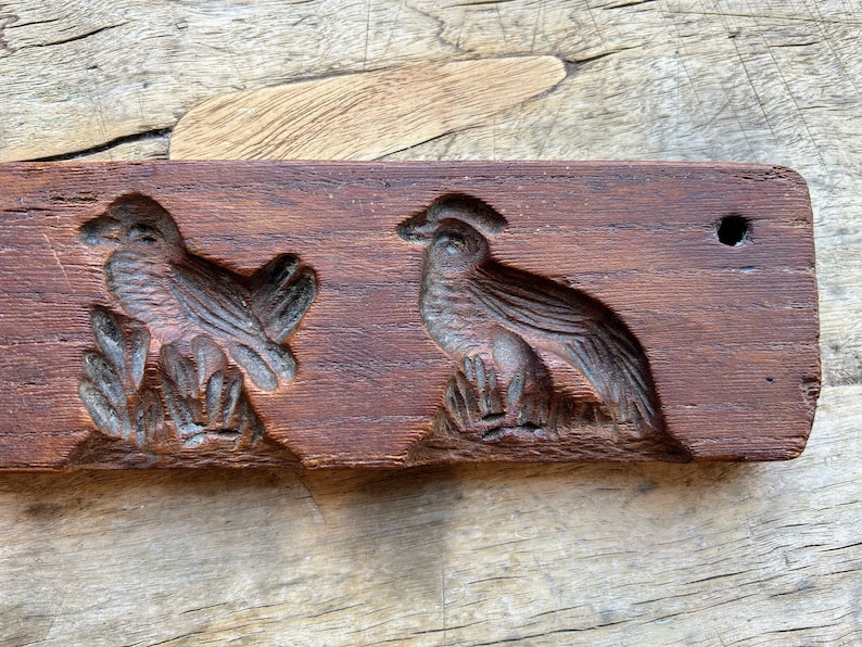 May include: Antique wooden cookie cutter with two bird designs. The cutter is brown and has a hole in the top.