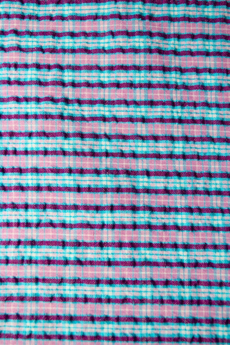 K&ouml;nnte beinhalten: Ein Nahaufnahme eines rosa und blauen karierten Stoffes mit einer strukturierten Oberfl&auml;che.