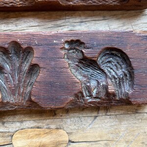 May include: Antique wooden mold for making cookies or candy. The mold features a rooster and a floral design. The wood is dark brown and has a rustic appearance.