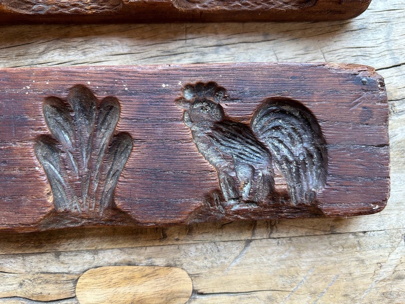 May include: Antique wooden mold for making cookies or candy. The mold features a rooster and a floral design. The wood is dark brown and has a rustic appearance.