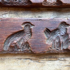 May include: A vintage wooden cookie mold with two bird designs. The mold is made of dark brown wood and has a worn, rustic appearance.