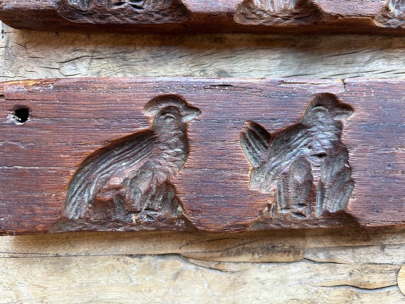May include: A vintage wooden cookie mold with two bird designs. The mold is made of dark brown wood and has a worn, rustic appearance.