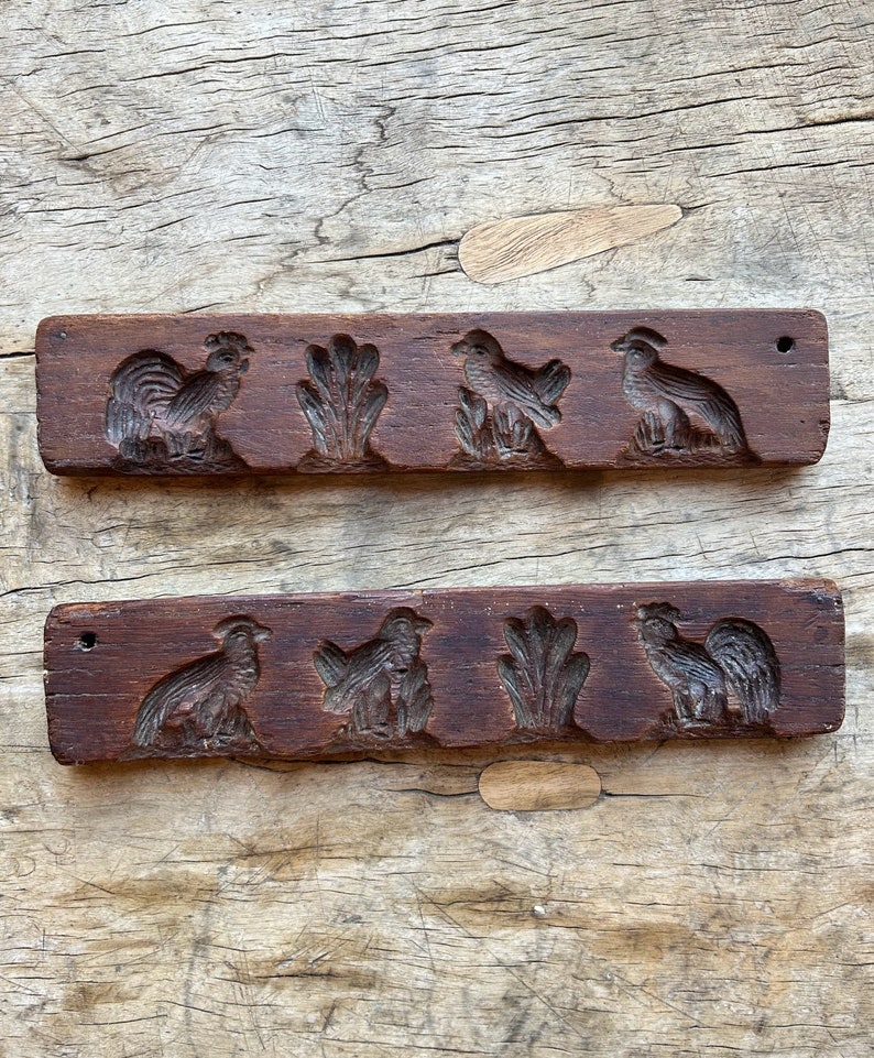 May include: Two antique wooden cookie cutters with raised designs of birds and a leafy plant. The cutters are brown and have a worn, rustic look.