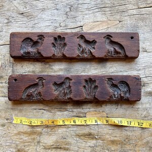 May include: Two vintage wooden cookie cutters with carved designs of roosters and birds. The cutters are brown and have a rustic look.
