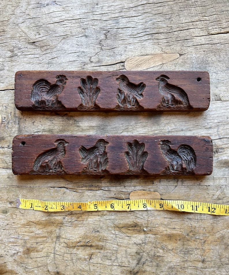 May include: Two vintage wooden cookie cutters with carved designs of roosters and birds. The cutters are brown and have a rustic look.