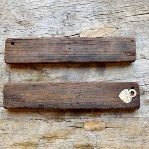 May include: Two rustic wooden signs with a distressed brown finish. The top sign has a small hole in the top left corner. The bottom sign has a small, heart-shaped tag with a metal ring attached to the right side.