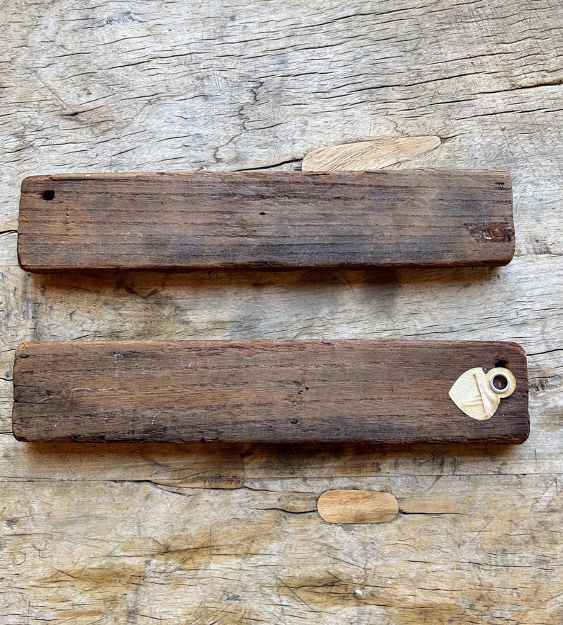 May include: Two rustic wooden signs with a distressed brown finish. The top sign has a small hole in the top left corner. The bottom sign has a small, heart-shaped tag with a metal ring attached to the right side.