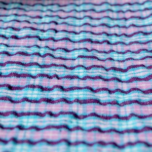 K&ouml;nnte beinhalten: Nahaufnahme eines strukturierten Stoffes mit einem wellenf&ouml;rmigen Muster. Der Stoff ist blau, lila und wei&szlig;.