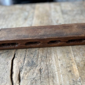 May include: A wooden rectangular box with five carved slots. The box is brown and has a worn, rustic appearance.