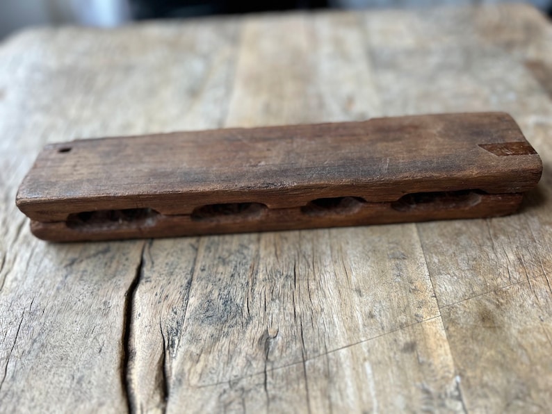 May include: A wooden rectangular box with five carved slots. The box is brown and has a worn, rustic appearance.