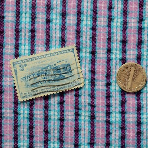 K&ouml;nnte beinhalten: Eine blaue und wei&szlig;e Briefmarke der Vereinigten Staaten mit einem Zug darauf und dem Text "3&cent;" und "The Baltimore & Ohio Railroad 125 Years of Transportation 1827-1952". Eine Silberm&uuml;nze mit dem Text "Liberty" und "In God We Trust" liegt auf einem rosa-blauen karierten Stoff.