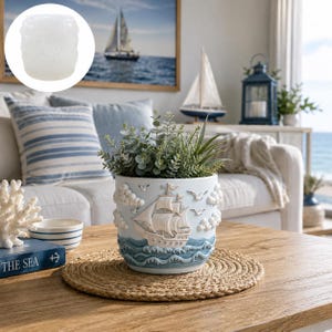 Könnte beinhalten: Hellblauer Blumentopf mit nautischem Thema, mit detailliertem Relief eines Segelschiffs, Wolken und Wellen. Der Topf ist mit Grünzeug gefüllt und steht auf einer gewebten Matte. Das Thema ist Küstendekoration.