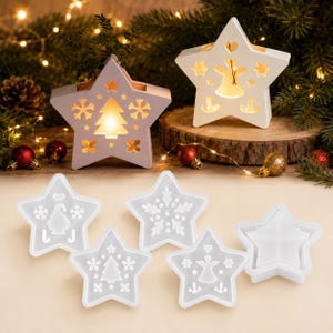Könnte beinhalten: Zwei sternförmige Leuchtdekorationen mit Ausschnitten eines Weihnachtsbaums und eines Engels, begleitet von fünf durchscheinenden Silikonformen in Sternform mit geprägten Motiven von Schneeflocken, einem Wichtel, einem Baum und einem Engel.