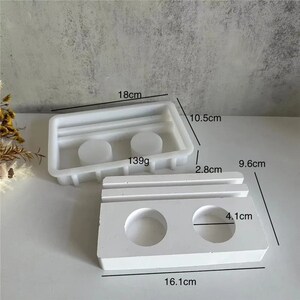May include: Two white silicone molds for making resin crafts. The larger mold is 18 cm by 10.5 cm and has two round depressions. The smaller mold is 16.1 cm by 9.6 cm and has two round depressions. Both molds have a 2.8 cm high ridge.