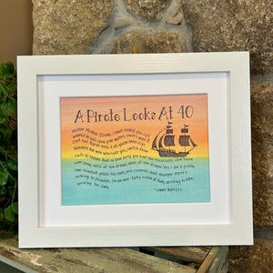 May include: A framed print with a watercolor background and black text. The text reads "A Pirate Looks At 40" and includes a quote from Jimmy Buffett about the ocean and pirates.
