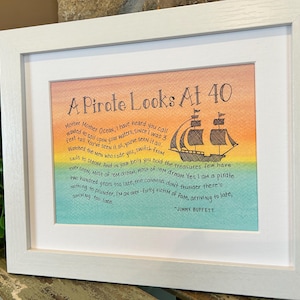 May include: A framed print with a watercolor background in shades of yellow, orange, green, and blue. The print features a black and white illustration of a pirate ship with the text "A Pirate Looks At 40" and a quote from Jimmy Buffett: "Mother Mother Ocean, I have heard you call wanted to sail upon your waters, since I was 3 Feel tall. You've seen it all, you've seen it all. Watched the men who rade you, switch from sails to steam. And in your belly you hold the treasures few have ever seen. Most of 'em dream, Most of 'em dream. Yes I am a pirate two hundred years too late, the cannons don't thunder there's nothing to plunder, I'm an over-forty victim of fate, arriving to late, arriving too late."