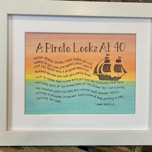 May include: A framed print with a watercolor background of orange, yellow, green, and blue. The print features a black and white illustration of a pirate ship and a poem titled "A Pirate Looks At 40" by Jimmy Buffett. The poem reads: "Mother Mother Ocean, I have heard you call wanted to sail upon your waters, since I was 3 feet tall. You've seen it all, you've seen it all. Watched the men who rode you switch from sails to steam. And in your belly you hold the treasures few have ever seen. Most of 'em dream, Most of 'em dream. Yes I am a pirate two hundred years too late, the cannons don't thunder there's nothing to plunder, I'm an over-forty victim of fate, arriving to late, arriving too late. - Jimmy Buffett"