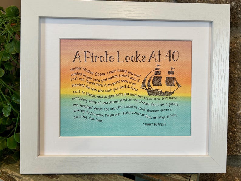 May include: A framed print with a watercolor background of orange, yellow, green, and blue. The print features a black and white illustration of a pirate ship and a poem titled "A Pirate Looks At 40" by Jimmy Buffett. The poem reads: "Mother Mother Ocean, I have heard you call wanted to sail upon your waters, since I was 3 feet tall. You've seen it all, you've seen it all. Watched the men who rode you switch from sails to steam. And in your belly you hold the treasures few have ever seen. Most of 'em dream, Most of 'em dream. Yes I am a pirate two hundred years too late, the cannons don't thunder there's nothing to plunder, I'm an over-forty victim of fate, arriving to late, arriving too late. - Jimmy Buffett"