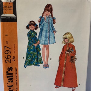 May include: A vintage sewing pattern for a child's robe in three styles. The pattern is for sizes 8 and includes instructions for a blue and white gingham robe, a floral print robe, and a red robe with a cat.