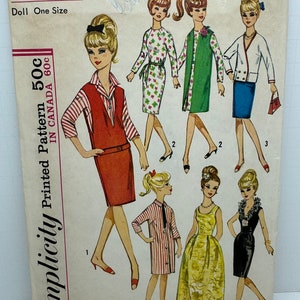 May include: Simplicity sewing pattern 5673 for dolls, one size. The pattern includes five different outfits: a red and white striped dress, a red dress with a vest, a green dress with a vest, a floral dress, and a white jacket with a blue skirt. The pattern is printed on white paper with black text.
