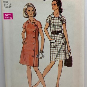 Könnte beinhalten: Vintage Simplicity Schnittmuster mit zwei Kleiderdesigns. Das Muster ist Größe 14, mit 91 cm Brustumfang. Das Cover ist grün und weiß mit Kleiderillustrationen. Der Text "NEW Sizing" ist sichtbar.
