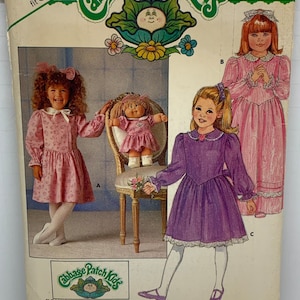 May include: A vintage sewing pattern for Cabbage Patch Kids dolls. The pattern includes three different dress designs: a pink dress with a white collar, a purple dress with a white collar, and a pink dress with a white collar and lace trim. The pattern is for sizes 5-6-6X and includes iron-on transfers.