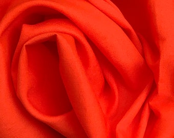 Op de afbeelding: Close-up van een feloranje stof met een gladde textuur. De stof is gevouwen en gedrapeerd, waardoor zachte plooien en bochten ontstaan.