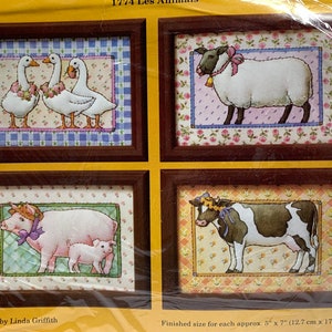 Può includere: Quattro motivi di punto croce incorniciati con animali da fattoria. I motivi includono un gruppo di tre oche, una pecora, un maiale con un maialino e una mucca. Ogni motivo è incorniciato da una cornice marrone con un passepartout bianco e uno sfondo floreale.