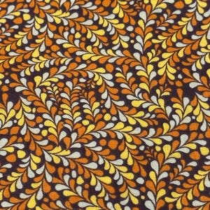 Op de afbeelding: Een bruine stof met een herhalend patroon van witte, gele en oranje druppelvormen. De druppelvormen zijn diagonaal gerangschikt.