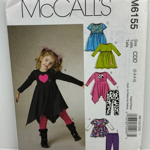 Puede incluir: Patrón de costura McCall's M6155 para ropa de niños. El patrón incluye diseños de vestidos y leggings. La portada presenta una foto de una niña con un vestido negro con un corazón rosa y leggings rojos. Tallas CDD (2-3-4-5).