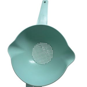 May include: A light teal colander with a handle and a perforated bowl. The colander has a handle with a hole for hanging and a small foot on the opposite side of the handle.