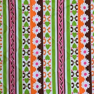 Peut inclure: Un tissu blanc avec un motif répété de rayures vertes, orange, brunes et roses. Les rayures sont décorées de petites fleurs blanches, de cœurs et d'un motif en chaîne.