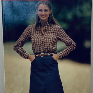 Peut inclure: Un patron de couture vintage de See & Sew par Butterick, mettant en scène une femme portant une chemise à carreaux et une jupe en jean. Le numéro du patron est 6882 et la taille est 14.