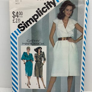 Può includere: Modello di cucito Simplicity numero 5532 per un abito. Il modello è per taglie da donna 14. Il modello include tre diversi stili di abiti. Il modello è su uno sfondo bianco con strisce blu e bianche.