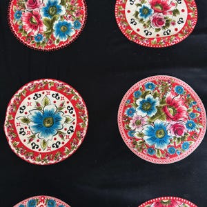 May include: A black fabric featuring a repeating pattern of circular motifs. Each circle displays a vibrant floral arrangement with blue and pink flowers, green leaves, and a red border with white and black decorative accents.