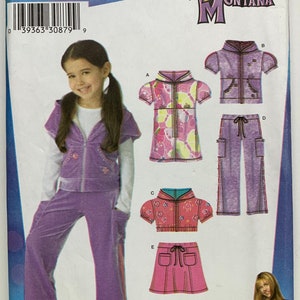 Puede incluir: Un patrón de costura para un atuendo de niña con una chaqueta con capucha morada, pantalones y una falda rosa. El patrón es de Simplicity y presenta el logotipo de Hannah Montana. El patrón es para las tallas 3-8.