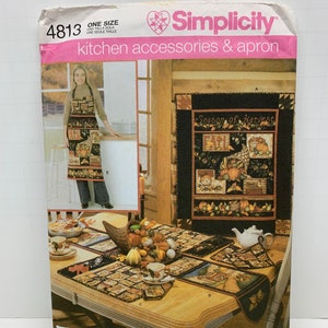 Op de afbeelding: Simplicity naaipatroon nummer 4813 voor keukenaccessoires en een schort. Het patroon bevat een wanddecoratie met de tekst "Season of Harvest", een tafelloper, placemats en een schort met zakken. Het patroon is voor één maat.