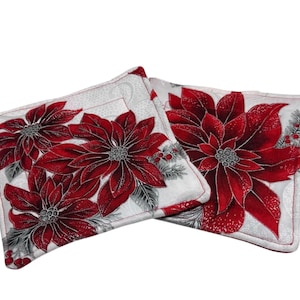 May include: Two square Christmas-themed pot holders. Each pot holder features a large red poinsettia flower with silver accents on a white background. The edges are trimmed with a red border.