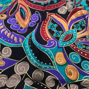 Puede incluir: Primer plano de una tela con un patrón de paisley en tonos de morado, turquesa, dorado y rojo sobre un fondo negro.